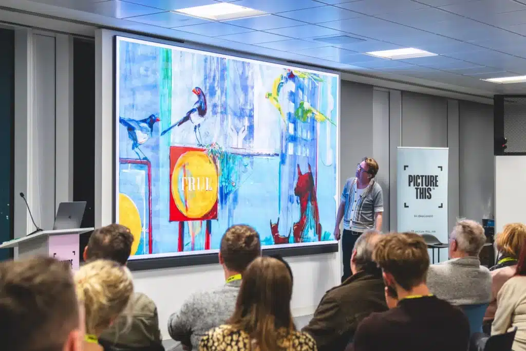 A speaker presenting artwork on screen to a seated audience